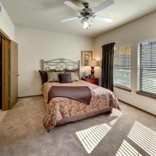 A cozy bedroom with a neatly made bed, ceiling fan, and ample natural light from large windows.