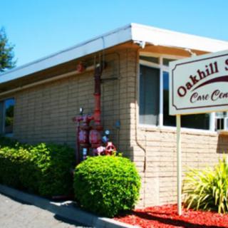 A brick building with a sign labeled 'Oakhill Care Center' surrounded by landscaping on a sunny day.