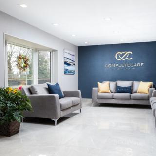 A modern waiting room featuring comfortable sofas, a wall display, and plant decor.