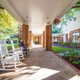 A serene outdoor walkway with rocking chairs and lush garden surroundings.