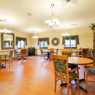 A well-lit dining area with round tables and wooden chairs, complemented by elegant chandeliers and decor.