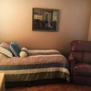 A cozy bedroom with a bed, pillows, recliner chair, and a painting on the wall.