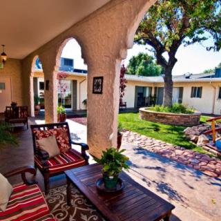 A sunny patio with comfortable seating, arches, and a view of a well-manicured garden courtyard.