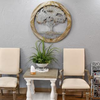 A cozy seating area featuring two beige chairs and a decorative table, complemented by a wall-mounted tree art piece and a potted plant for a touch of nature.