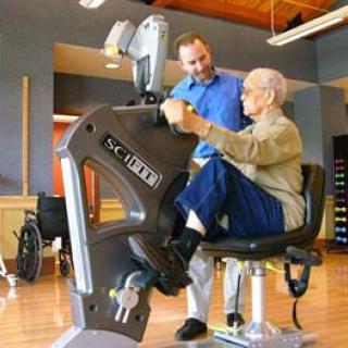 A healthcare professional assists an elderly person using a specialized exercise machine designed for rehabilitation and fitness.