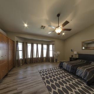 A spacious modern bedroom with a large bed, wooden wardrobe, and a ceiling fan.