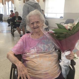 An elderly woman happily holding a bouquet of flowers while seated in a wheelchair.