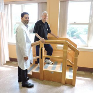 A doctor and a patient are engaged in rehabilitation exercises, using a stair model to assist with physical therapy.