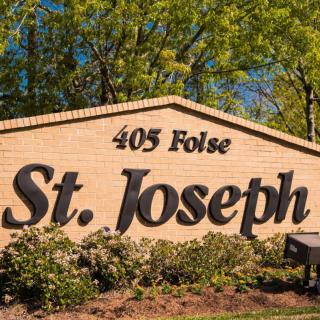 A brick sign for St. Joseph located at 405 Folse, surrounded by greenery.