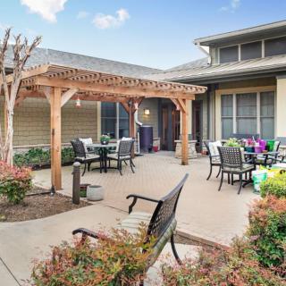 A cozy outdoor patio area featuring a wooden pergola, seating arrangements, and vibrant landscaping.