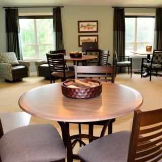 A cozy living room with multiple seating areas, featuring tables and chairs arranged near large windows.