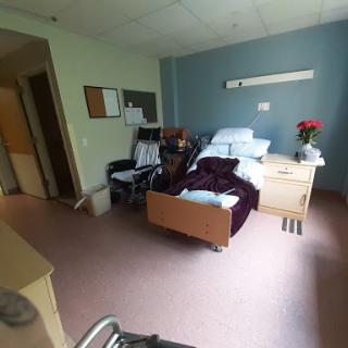 A spacious hospital patient room featuring a bed, wheelchair, and floral decor.