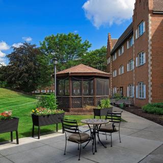 A peaceful outdoor patio area next to an apartment building with seating, a gazebo, and surrounding greenery.