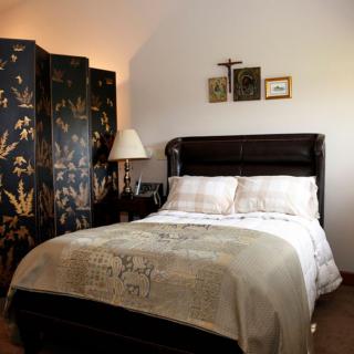 A cozy bedroom with a dark upholstered bed, decorative screen divider, and elegant lamp.