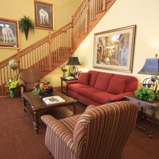 A cozy living room featuring a red sofa, striped armchair, and wooden staircase, adorned with artwork and decorative plants.