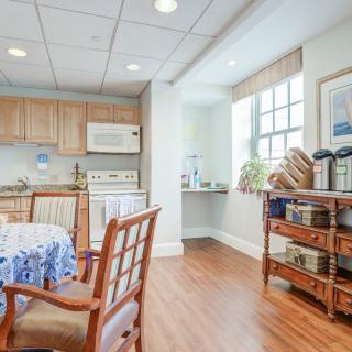 A cozy kitchen and dining area with wooden flooring, featuring a table set, kitchen cabinets, and appliances near a bright window.
