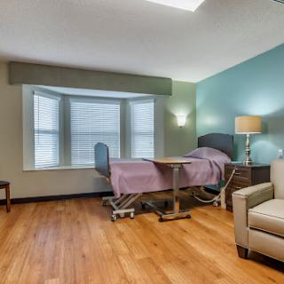 A well-lit hospital patient room featuring a bed, a window with blinds, and comfortable furniture.