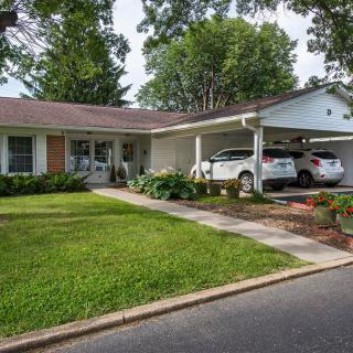 A suburban house with a well-maintained front yard and two cars parked under a carport.