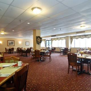 A spacious restaurant dining area with neatly arranged tables and chairs, featuring warm lighting and a carpeted floor.