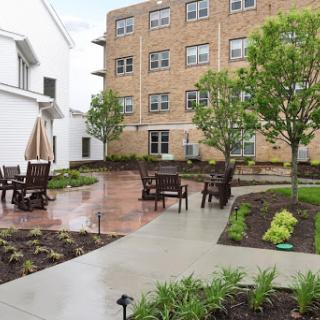 A serene courtyard featuring outdoor seating, surrounded by lush greenery and a residential building.