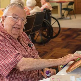 An elderly man engages in painting at a senior center, expressing his creativity.