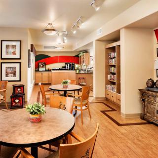 A cozy dining area with round tables and wooden chairs, leading into a kitchen with vibrant artwork and well-organized shelves.