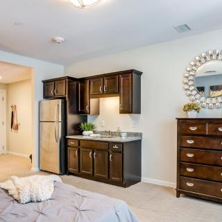 A cozy bedroom with a kitchenette, featuring brown cabinets and a stainless steel fridge.
