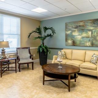 A cozy living room with a sofa, armchair, coffee table, and decorative elements including a painting and a large potted plant.