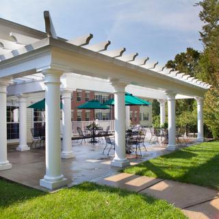 A scenic outdoor patio area with a pergola and green umbrella-shaded tables, surrounded by lush greenery.