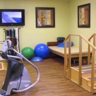A therapy room equipped with exercise machines, balance balls, and therapy stairs.