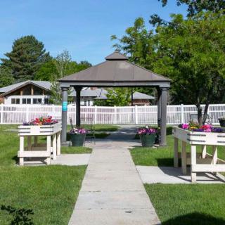 A serene garden with a pathway leading to a wooden gazebo, surrounded by flowers and trees.