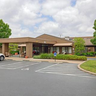 A building with a parking lot in front, surrounded by greenery under a cloudy sky.