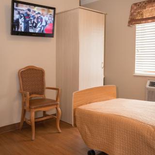 A cozy hospital room featuring a patient bed, television, and comfortable chair.