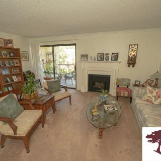 A cozy living room featuring a sofa, chairs, and a coffee table centered around a fireplace, with bookshelves and decorative elements enhancing the space.