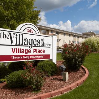 A senior living apartment complex with a landscaped entrance and visible building in the background.