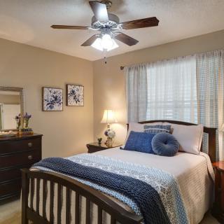 A cozy bedroom featuring a neatly made bed with blue and white linens, a dresser with a mirror, and a ceiling fan overhead.