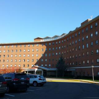 A curved brick building with multiple windows, surrounded by a parking lot on a sunny day.