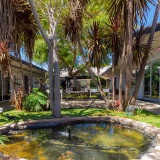 A sunny courtyard with a central fountain surrounded by palm trees and buildings.