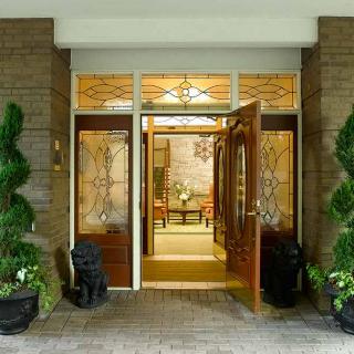 A luxurious entrance featuring an open wooden door, flanked by potted plants, leading into a well-decorated interior.
