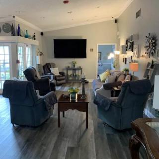 A cozy living room with armchairs arranged around a central coffee table, featuring a large television on the wall.