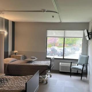 A hospital room with two medical beds, a window, and a television on the wall.