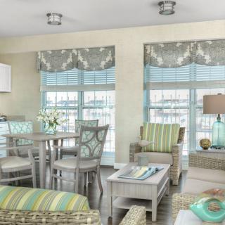 A cozy living and dining area with a coastal theme featuring pastel colors, striped furniture, and ample natural light filtering through the window blinds.