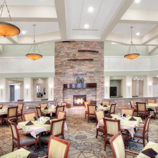 A spacious dining area featuring modern decor with a central fireplace surrounded by neatly arranged tables and chairs.