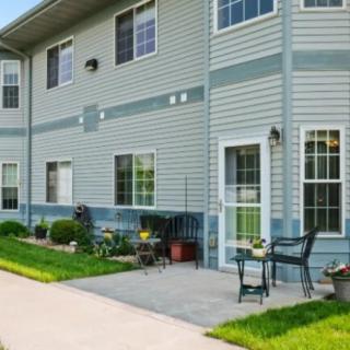 A residential building with a small patio and outdoor seating area surrounded by a green lawn.