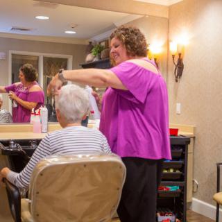 A hair stylist tends to an elderly client's hair in a cozy salon setting.