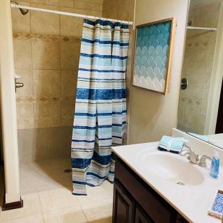 A bathroom featuring a shower with a blue and white striped curtain, a sink with toiletries, and a piece of artwork on the wall.