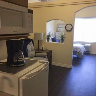 A view of a studio apartment featuring a compact kitchen area with a coffee maker and microwave, leading into a living space and bedroom.