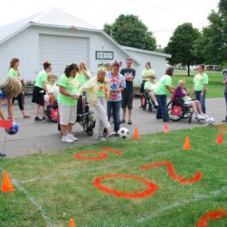 A lively community event where children and individuals in wheelchairs participate in various outdoor activities, surrounded by supportive peers.