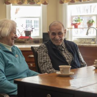 An elderly couple sitting at a kitchen table enjoying a conversation over tea.