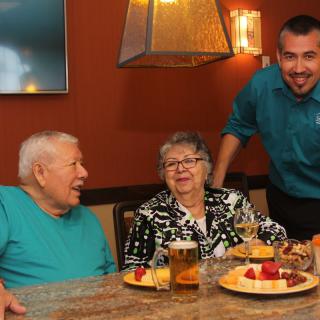 Seniors enjoying a meal at a restaurant with a friendly waiter.